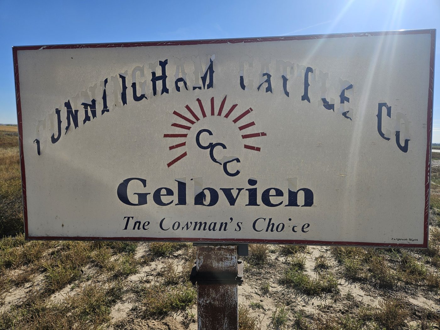 A weathered white sign with a red border reading Cunningham Cattle Co. in arched letters over a red sunburst and the letters CCC, with Gelbvieh and The Cowman's Choice below.